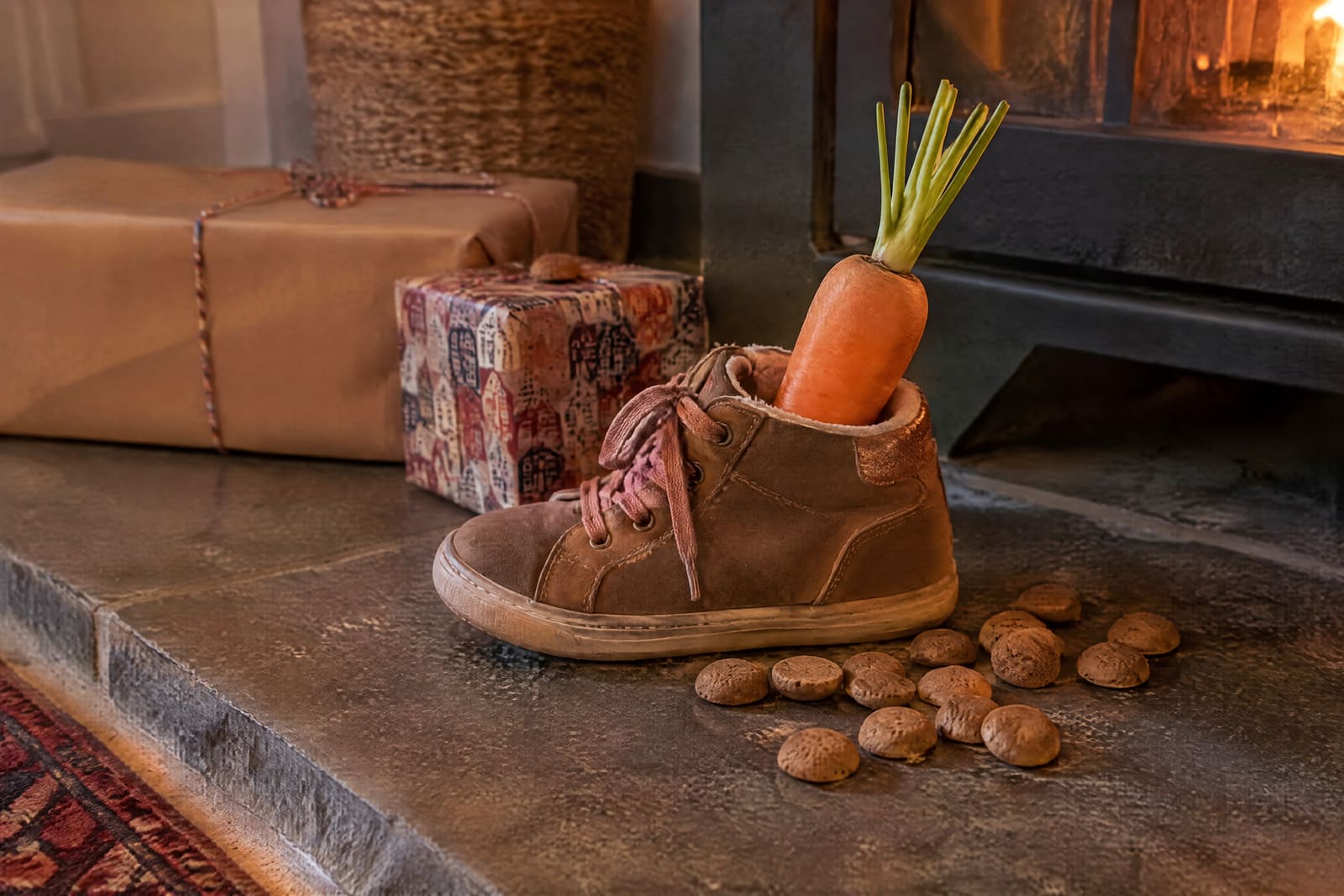 A child's shoe with a carrot by the fireplace, pepernoten and wrapped presents behind