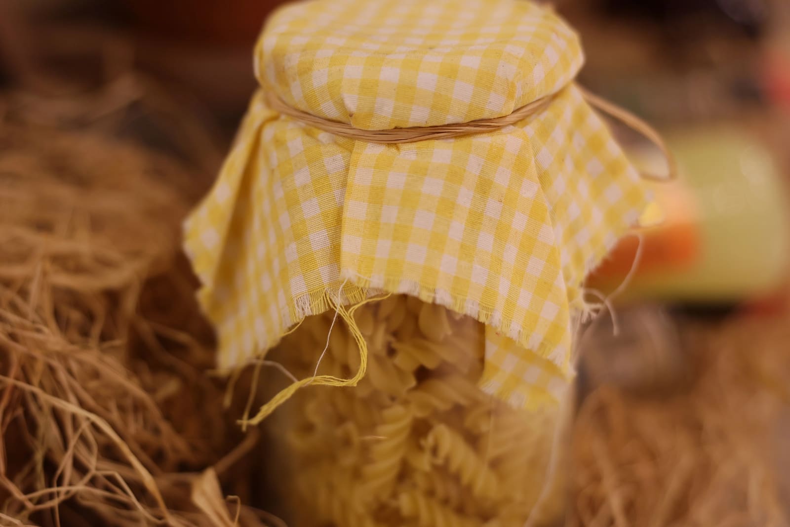 A jar of pasta with a yellow gingham cloth tied over its lid