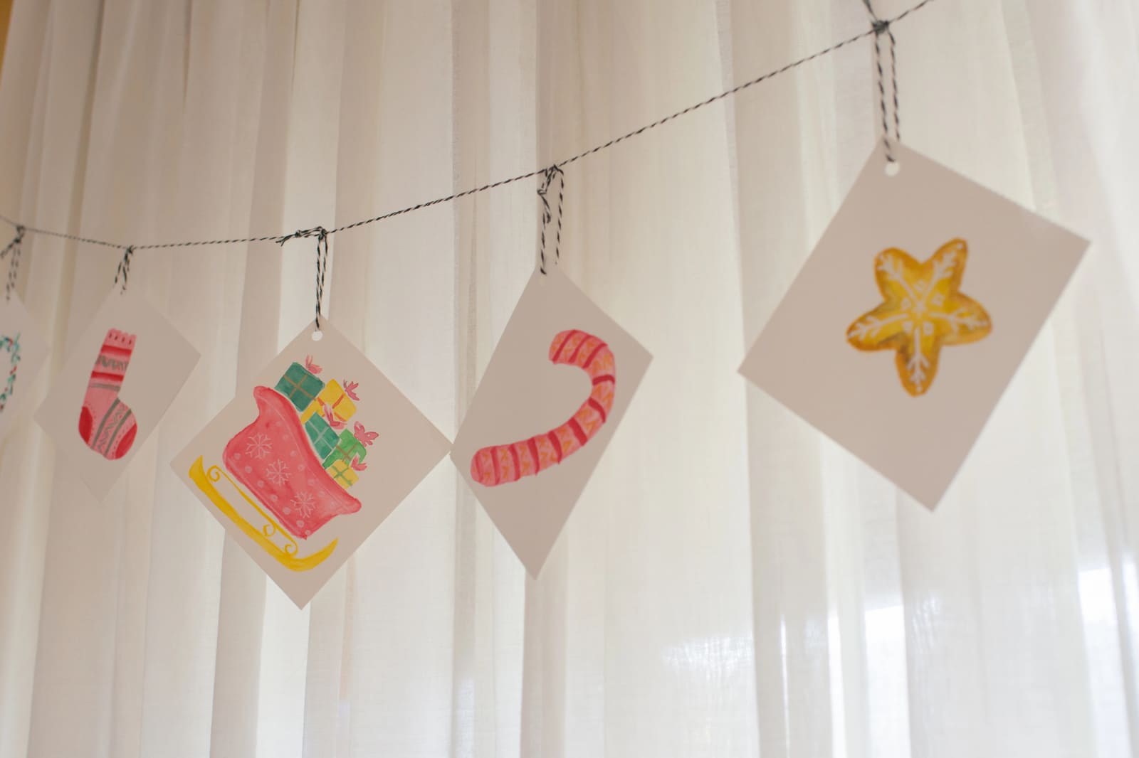 Tarjetas de Navidad pintadas a mano colgadas de un cordel ante una cortina
