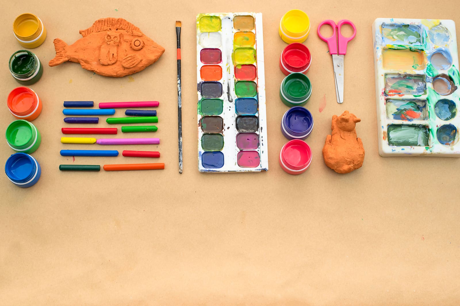 Pinturas, ceras, animales de arcilla y tijeras sobre papel marrón