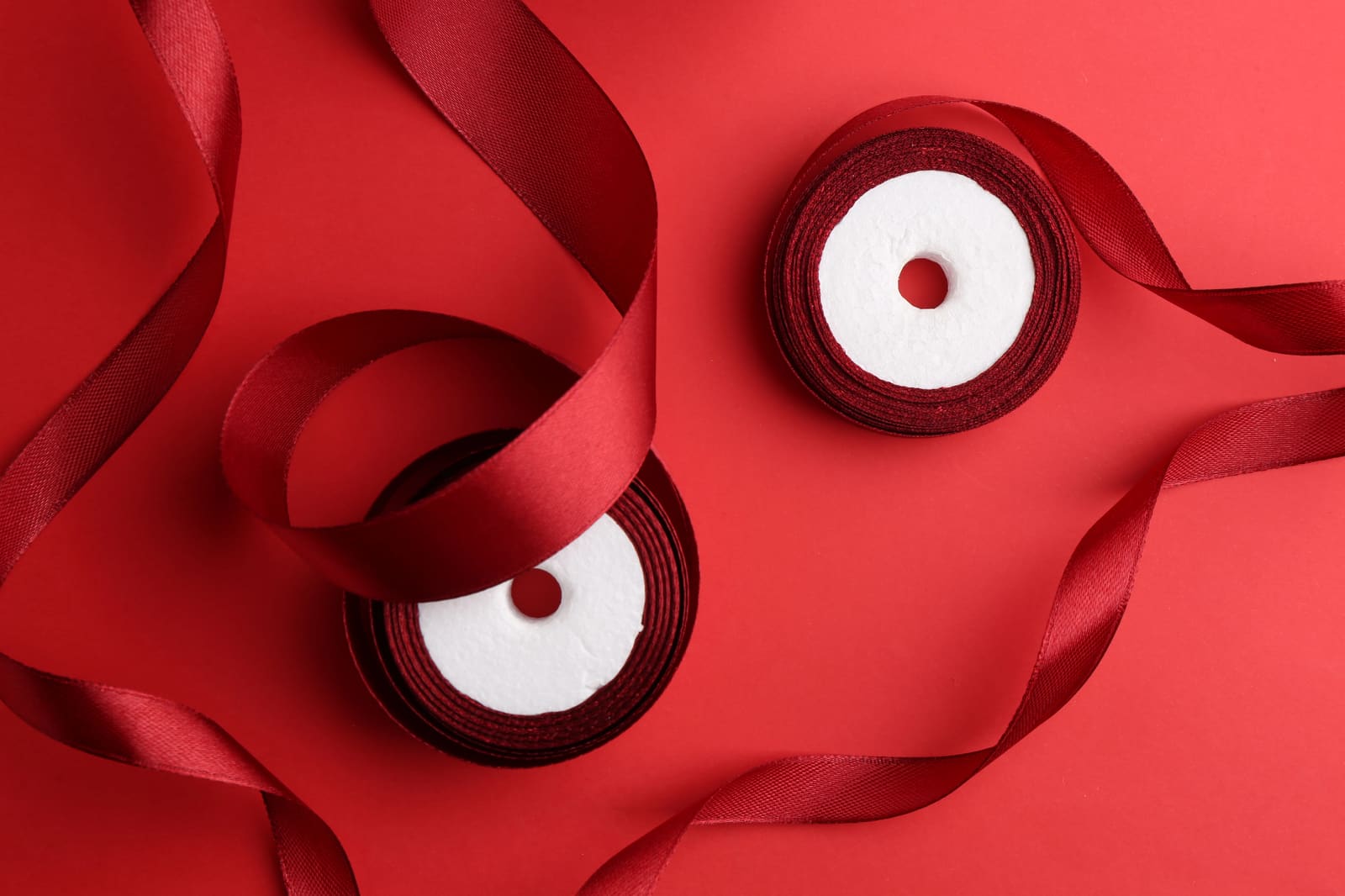 Two spools of red satin ribbon unrolled on a red background