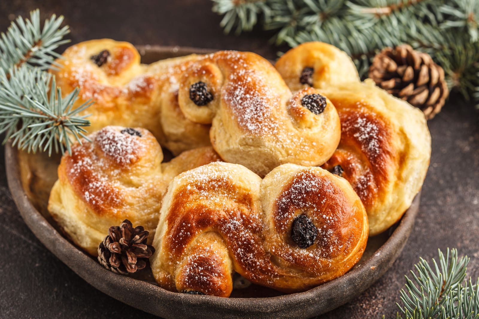 A bowl of saffron buns with raisins among fir sprigs and pine cones