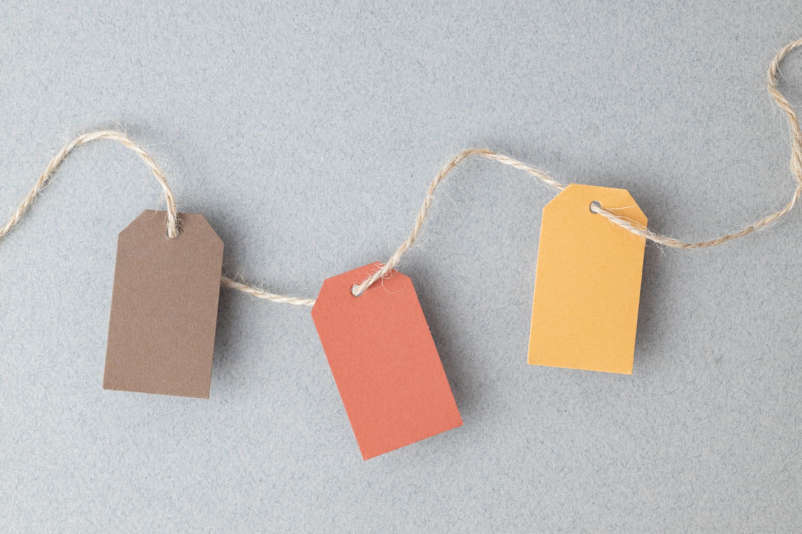 Three blank paper gift tags in brown, coral and yellow on twine