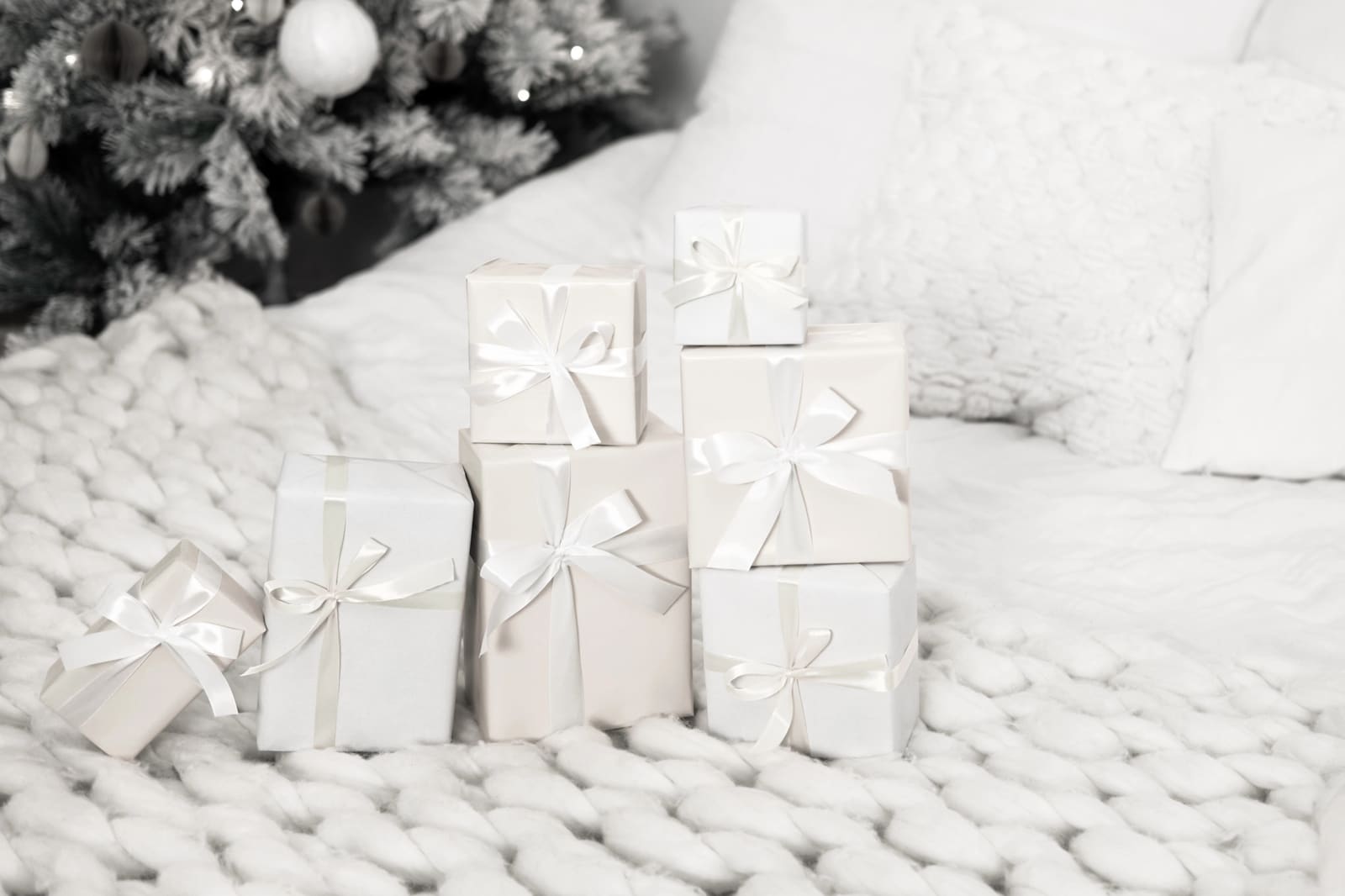 White gift boxes tied with white satin ribbon on a chunky knit blanket