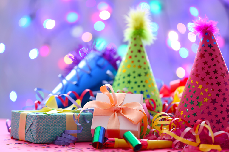 Birthday gifts on a table with party hats behind it