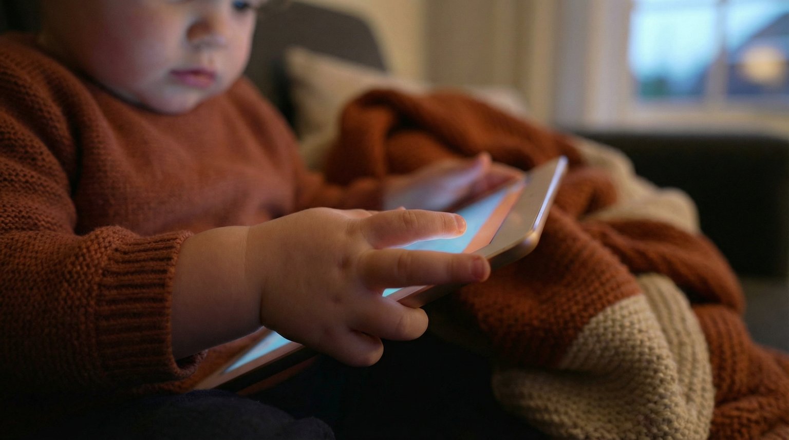 Small child's hands gripping tablet with screen glow reflecting on fingers