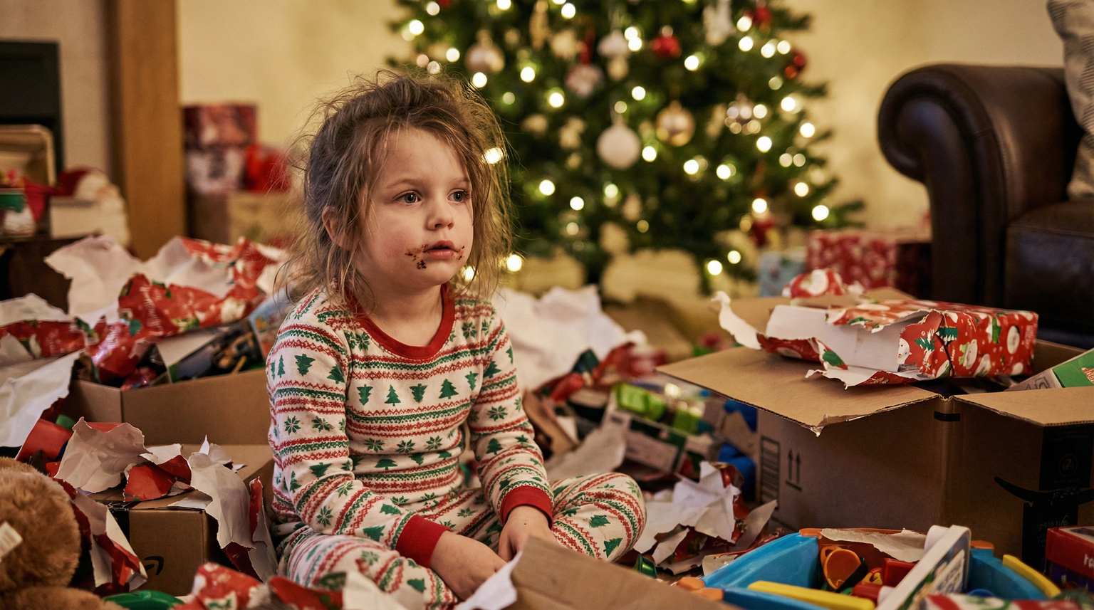 Five year old child sitting among large pile of opened Christmas presents looking overstimulated and glazed